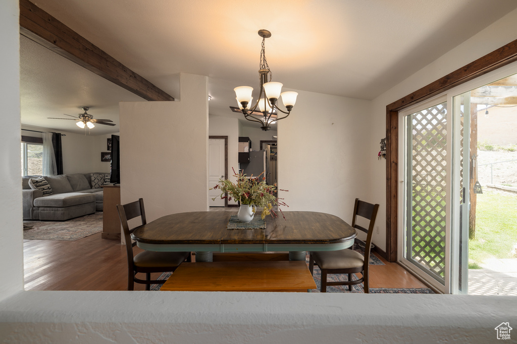 Dining space featuring wood finished floors, a chandelier, beamed ceiling, and ceiling fan