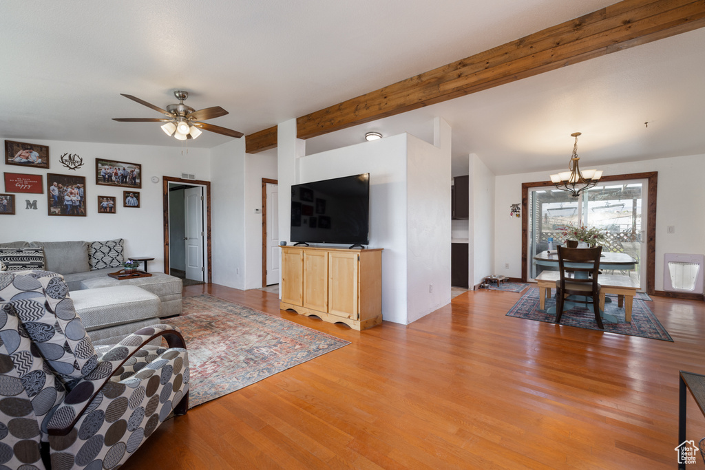 Living area featuring a chandelier, light wood-style flooring, a ceiling fan, and beam ceiling