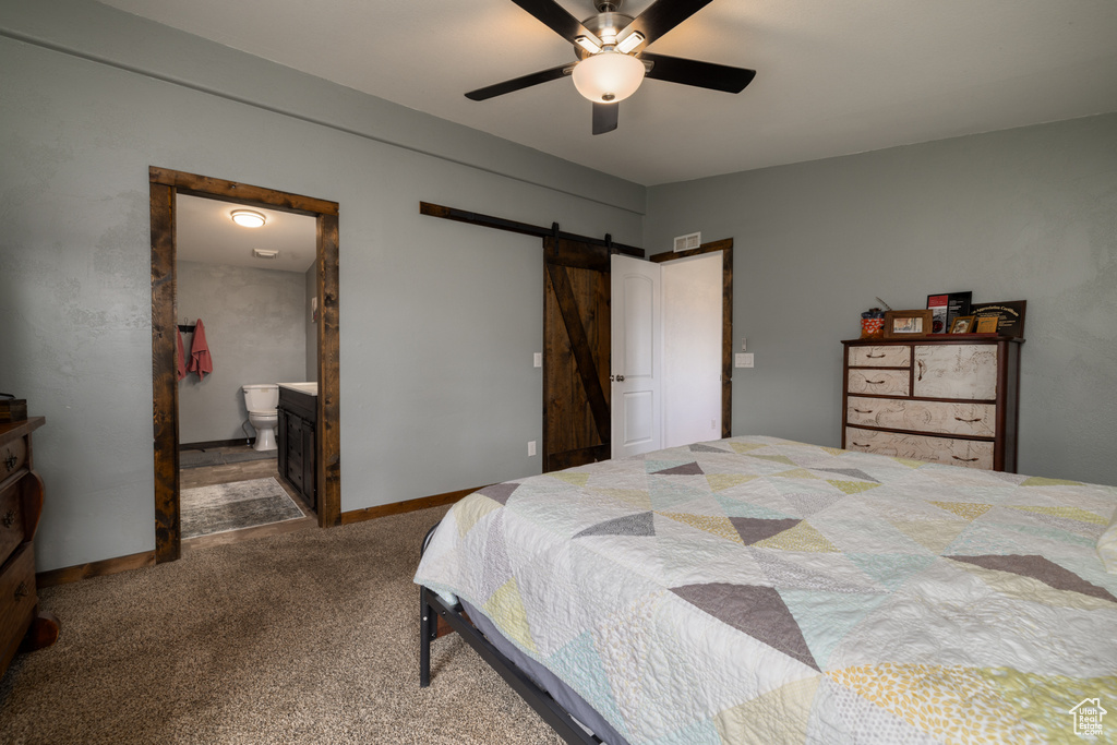 Carpeted bedroom with a barn door, ceiling fan, and connected bathroom