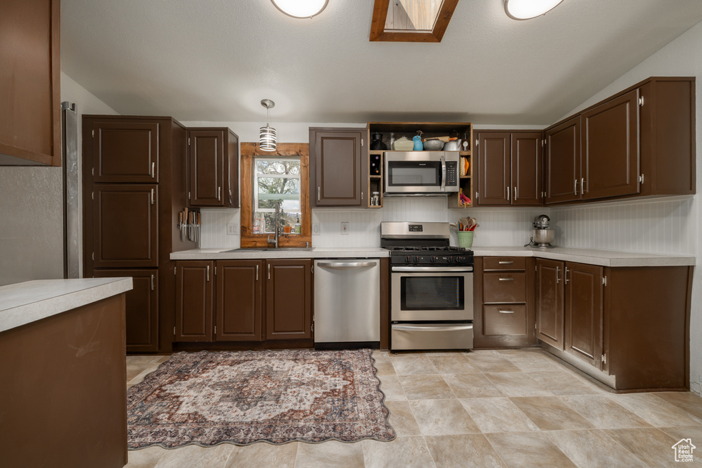 Kitchen featuring appliances with stainless steel finishes, a sink, light countertops, dark brown cabinetry, and vaulted ceiling