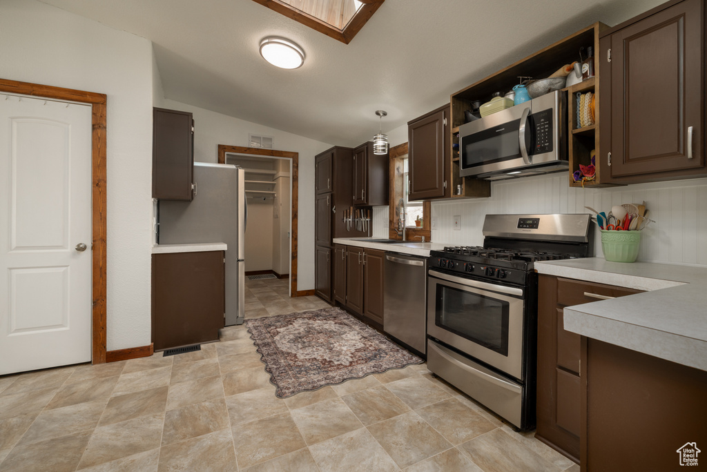 Kitchen with stainless steel appliances, light countertops, vaulted ceiling, dark brown cabinetry, and stone finish floors