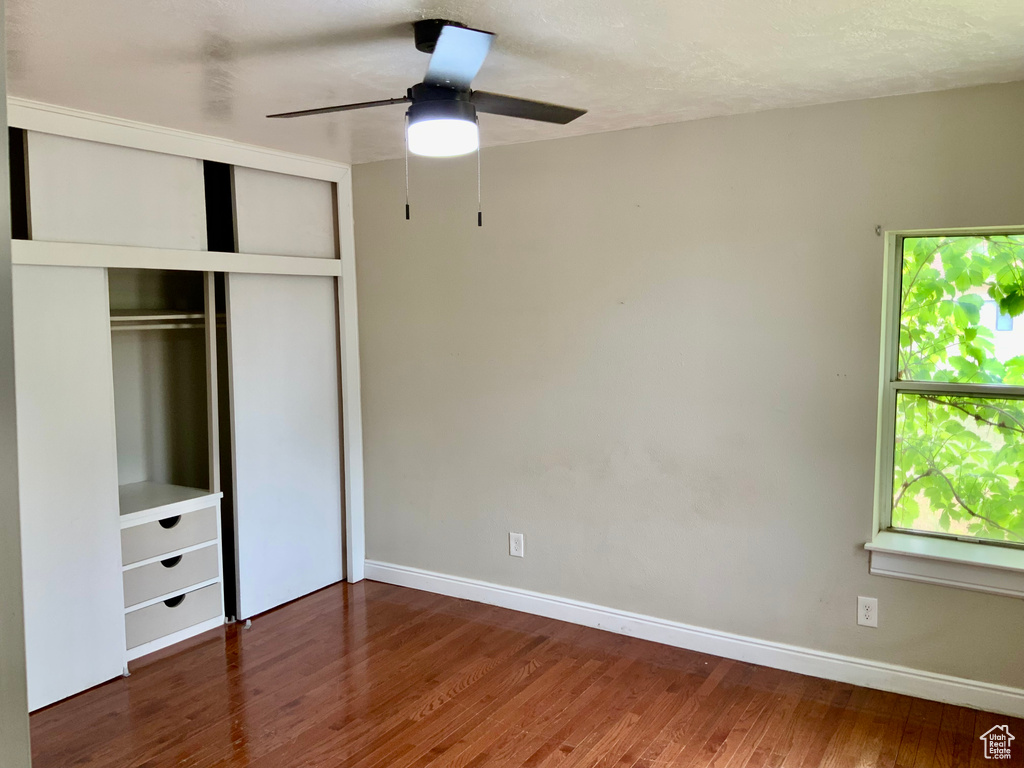 Unfurnished bedroom featuring wood finished floors, a closet, baseboards, and a ceiling fan