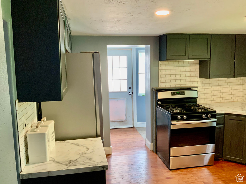Kitchen featuring stainless steel gas stove, tasteful backsplash, light wood finished floors, freestanding refrigerator, and light stone countertops