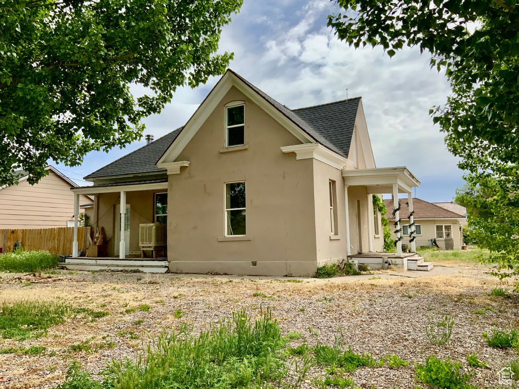 Back of house with covered porch, a shingled roof, stucco siding, and fence