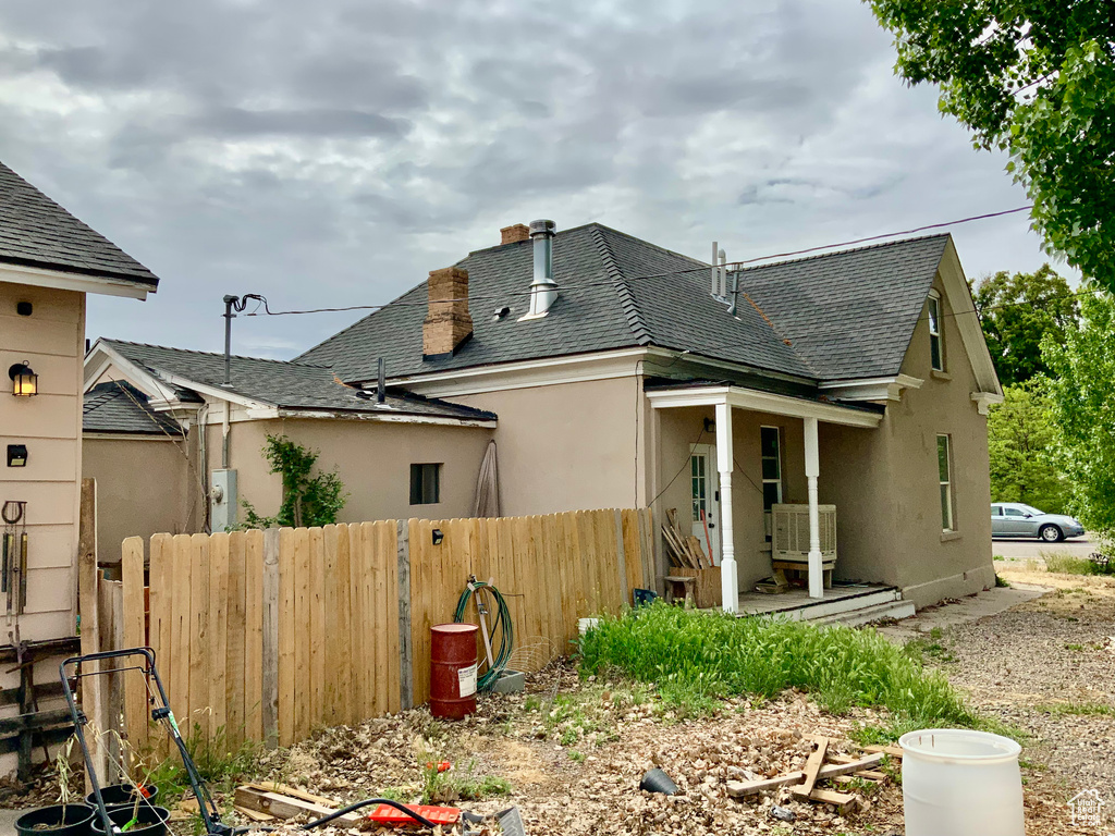 Rear view of house featuring fence, roof with shingles, and stucco siding