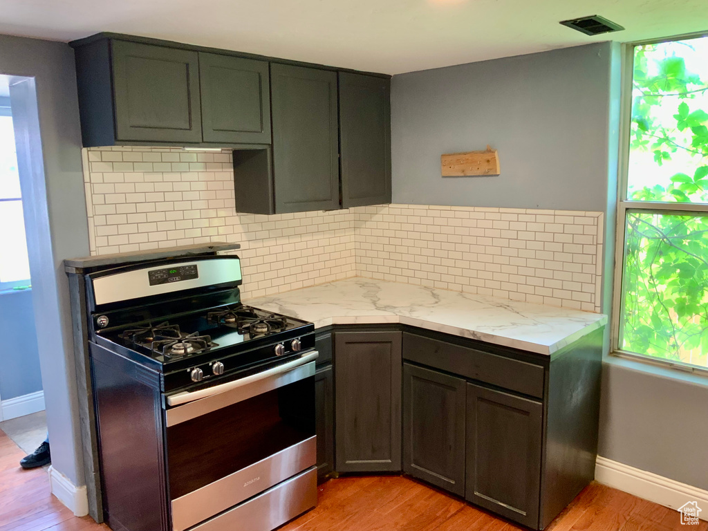 Kitchen featuring stainless steel gas range oven, plenty of natural light, light wood finished floors, and light stone counters