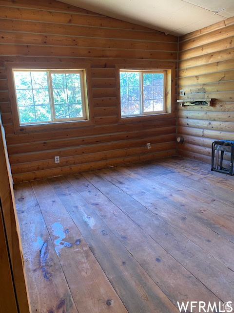 Unfurnished living room featuring rustic walls, hardwood / wood-style flooring, and vaulted ceiling