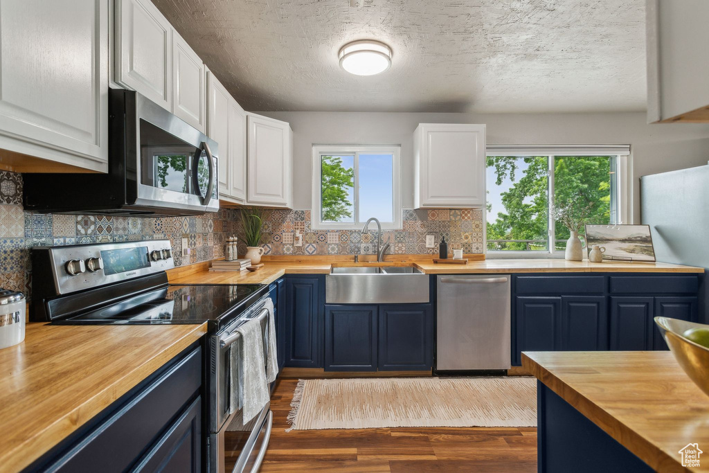 Kitchen with wood counters, appliances with stainless steel finishes, a sink, blue cabinets, and wood finished floors