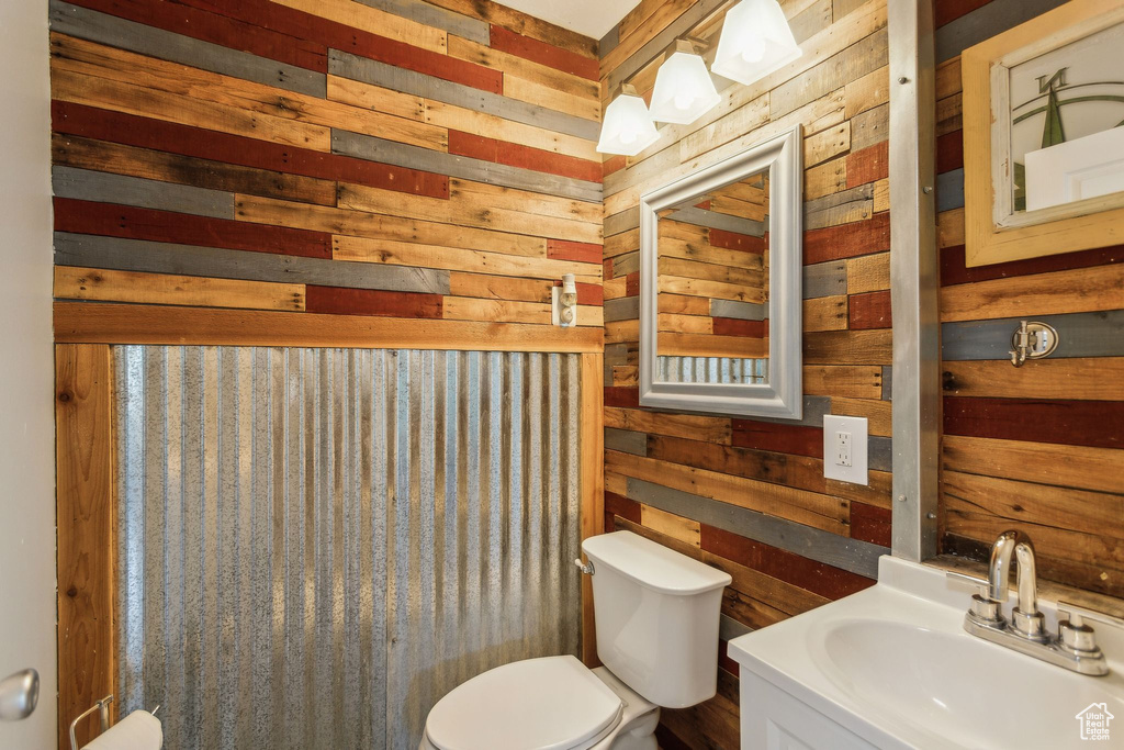 Half bathroom featuring wood walls, toilet, and vanity