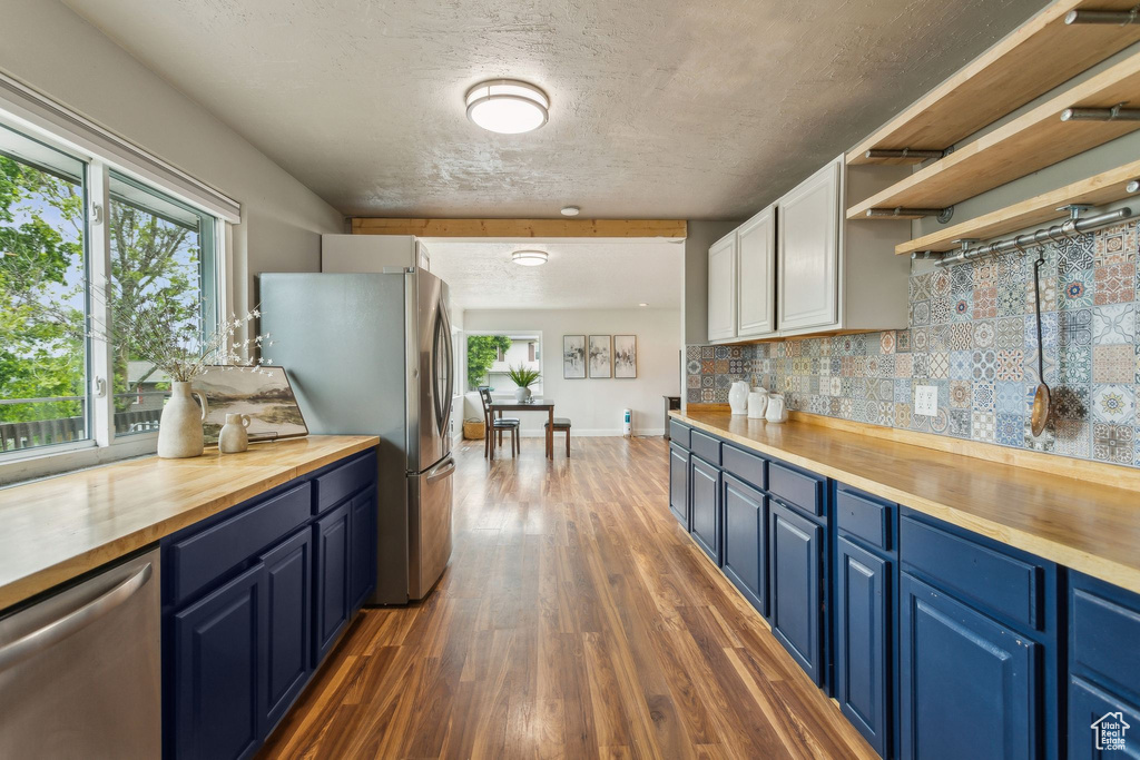 Kitchen featuring butcher block countertops, blue cabinets, stainless steel appliances, and dark wood-style floors