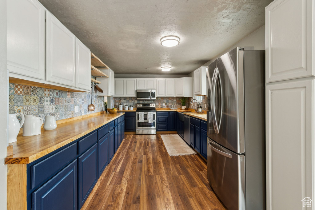 Kitchen featuring appliances with stainless steel finishes, blue cabinets, dark wood finished floors, white cabinetry, and wood counters