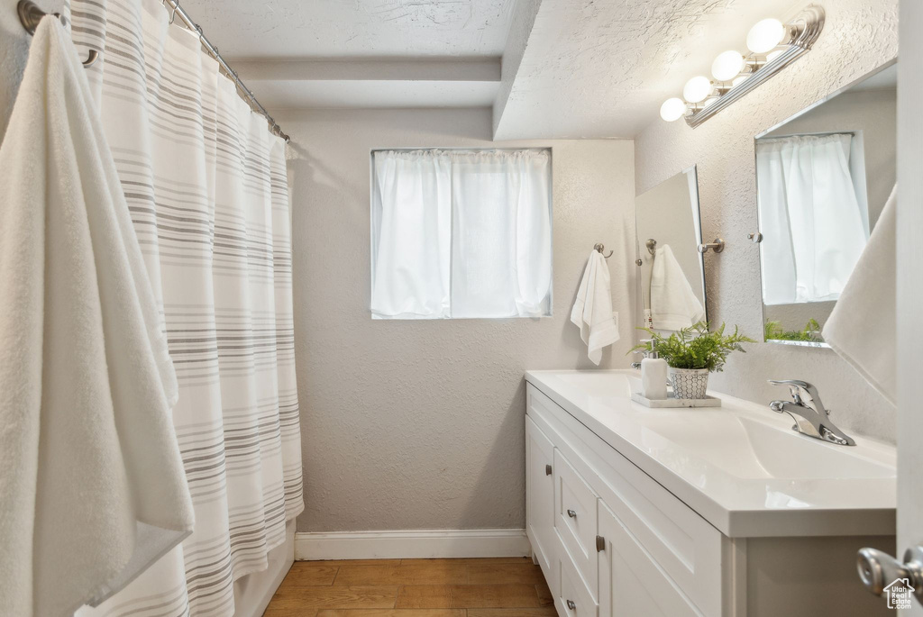 Full bathroom with baseboards, wood finished floors, double vanity, a shower with shower curtain, and a textured ceiling