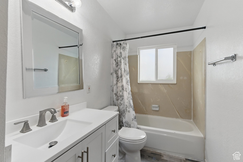 Bathroom with toilet, vanity, shower / tub combo, and wood finished floors