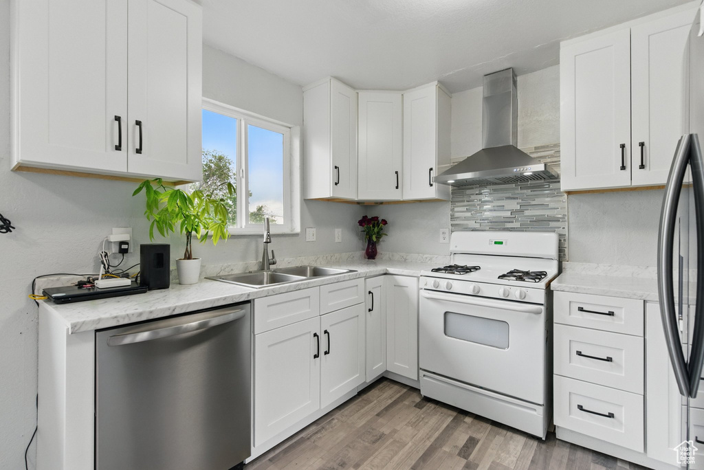 Kitchen featuring white gas stove, dishwasher, exhaust hood, a sink, and white cabinetry