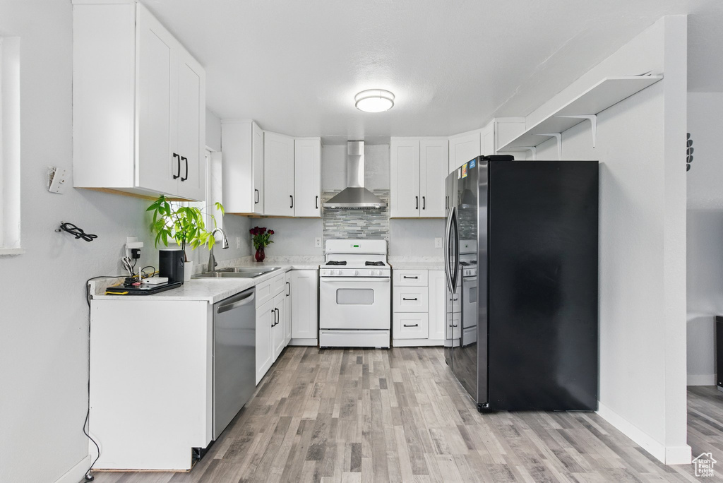 Kitchen with appliances with stainless steel finishes, wall chimney exhaust hood, a sink, light wood-style floors, and light countertops