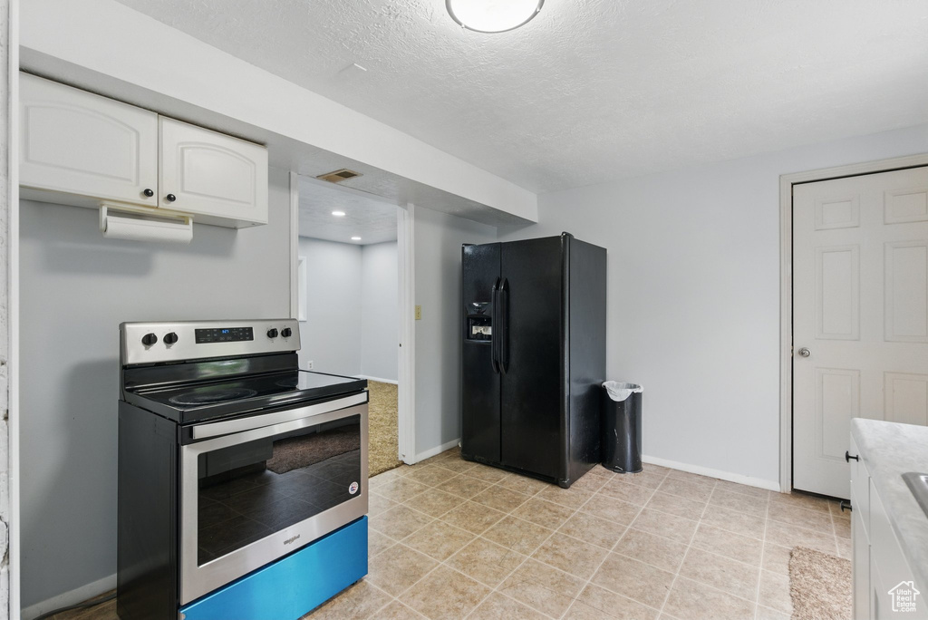 Kitchen featuring stainless steel electric range, black fridge with ice dispenser, white cabinets, light countertops, and baseboards