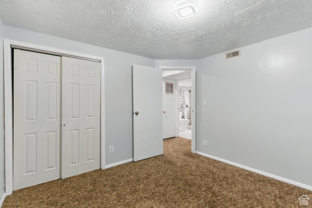 Unfurnished bedroom with carpet flooring, a closet, a textured ceiling, and baseboards