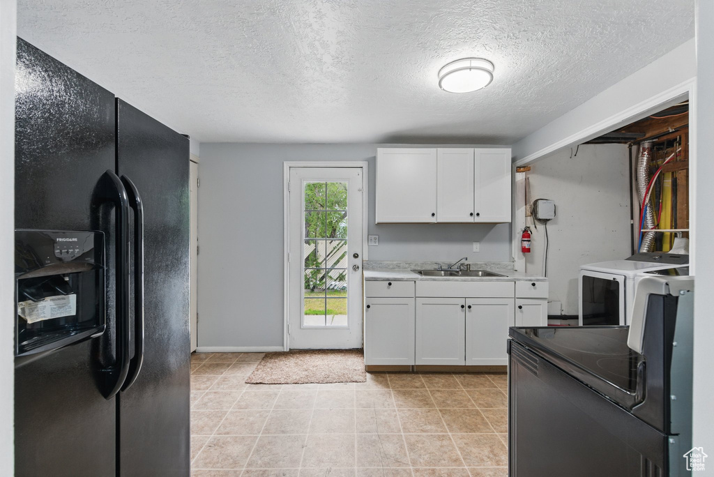 Kitchen with black appliances, washer / dryer, a sink, white cabinetry, and a textured ceiling