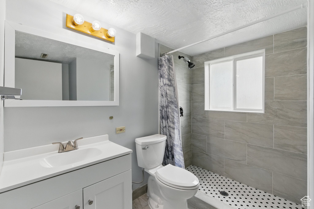 Full bath with a stall shower, vanity, toilet, a textured ceiling, and baseboards