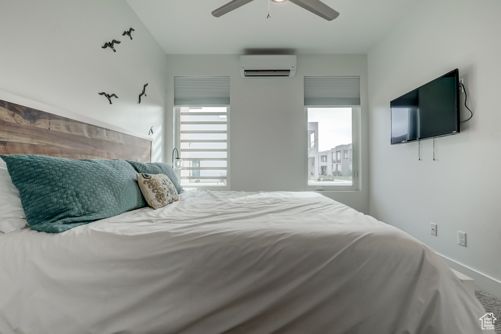 Bedroom with a wall unit AC, multiple windows, ceiling fan, and baseboards