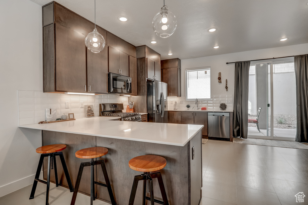 Kitchen with appliances with stainless steel finishes, a peninsula, a kitchen bar, tasteful backsplash, and light countertops