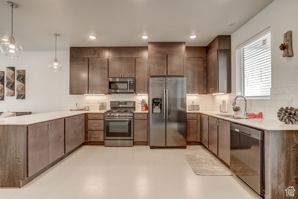 Kitchen with stainless steel appliances, a sink, a peninsula, backsplash, and light countertops