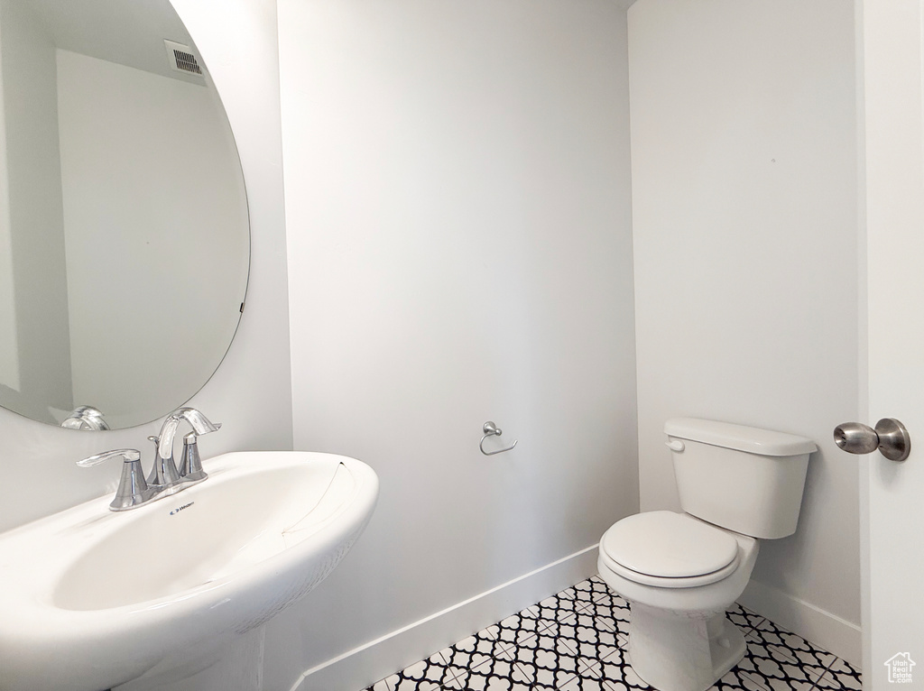 Half bath with baseboards, a sink, toilet, and tile patterned floors