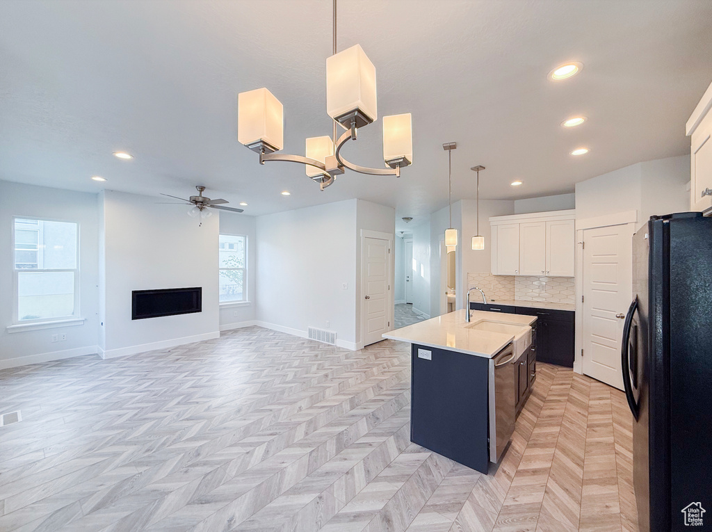 Kitchen featuring freestanding refrigerator, a ceiling fan, a kitchen island with sink, light countertops, and recessed lighting