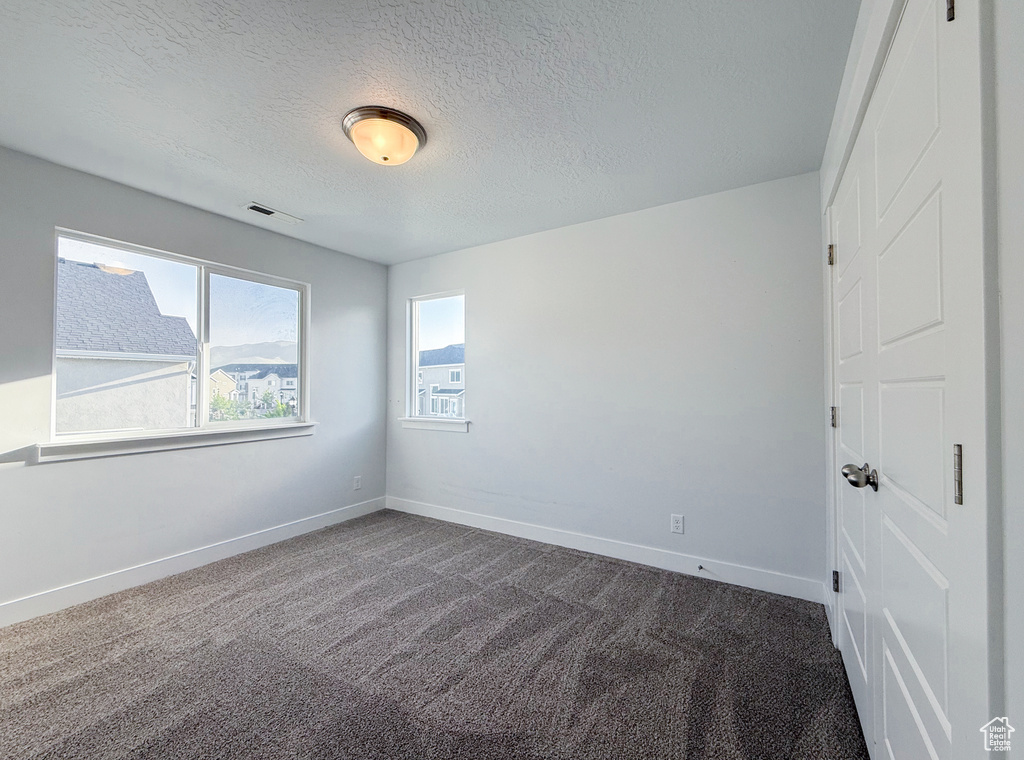 Unfurnished room featuring dark colored carpet, baseboards, and a textured ceiling