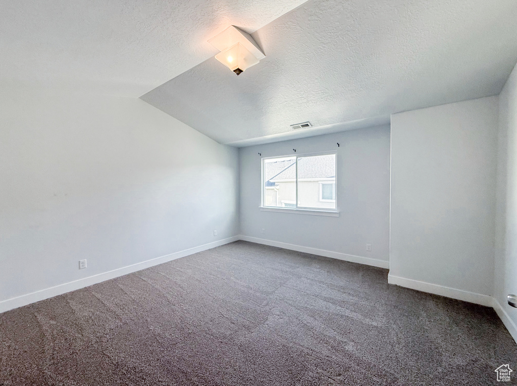 Unfurnished room with carpet, a textured ceiling, baseboards, and vaulted ceiling