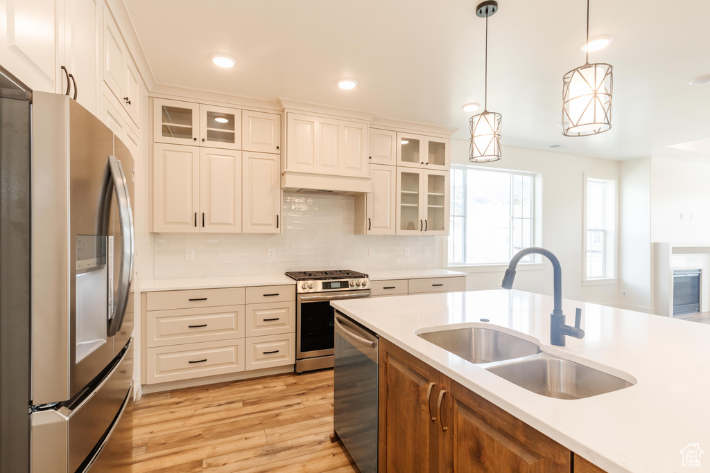 Kitchen with stainless steel appliances, light countertops, a sink, light wood finished floors, and hanging light fixtures