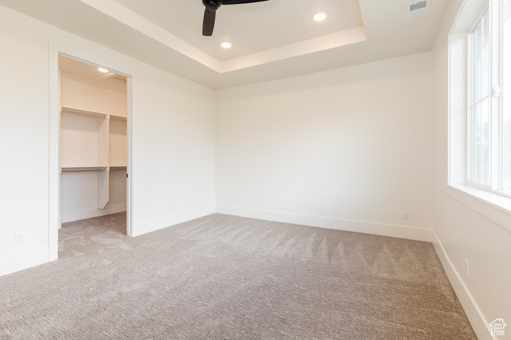 Unfurnished bedroom with carpet floors, a walk in closet, recessed lighting, a raised ceiling, and baseboards