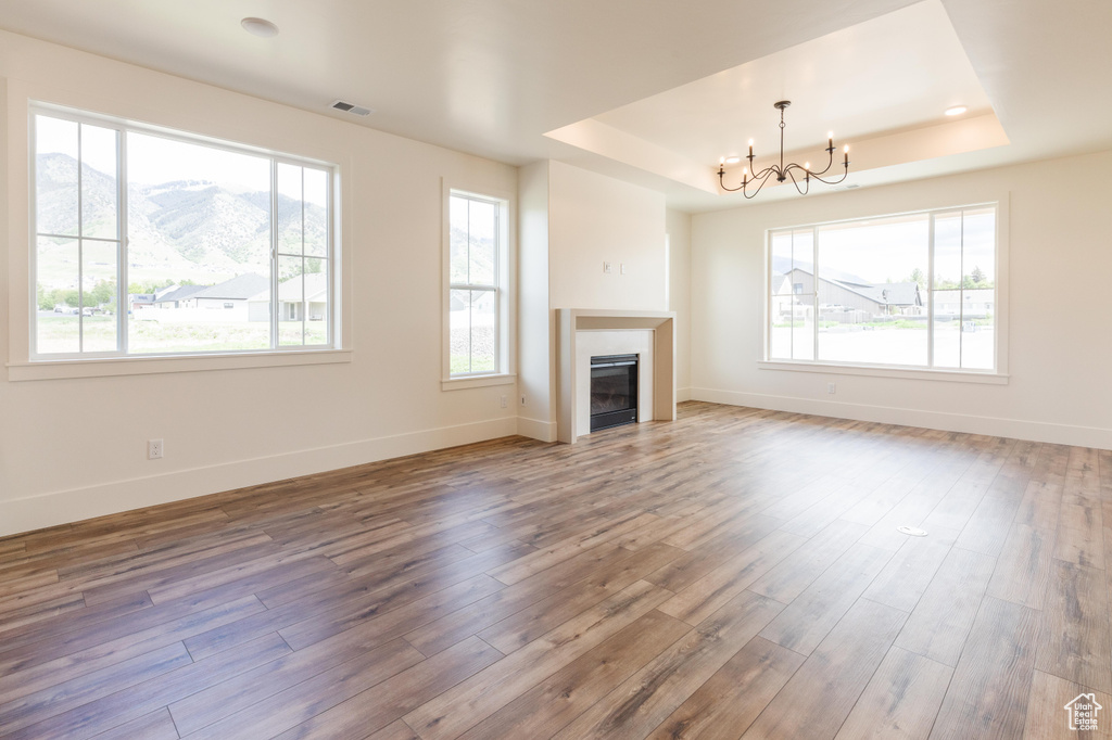 Unfurnished living room featuring a raised ceiling, hardwood / wood-style floors, a chandelier, baseboards, and a glass covered fireplace