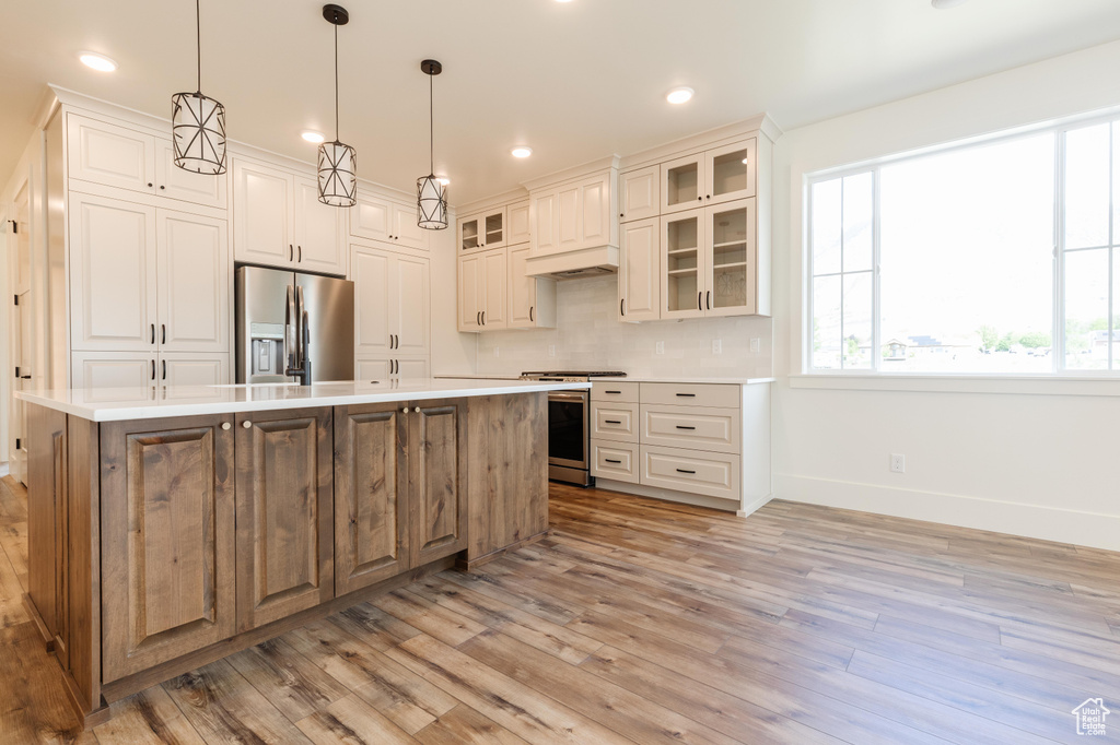 Kitchen featuring appliances with stainless steel finishes, baseboards, light wood-type flooring, a kitchen island with sink, and decorative backsplash