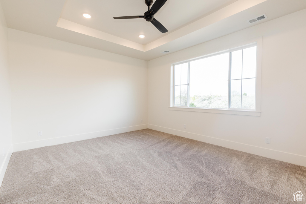 Carpeted spare room featuring baseboards, a raised ceiling, recessed lighting, and a ceiling fan