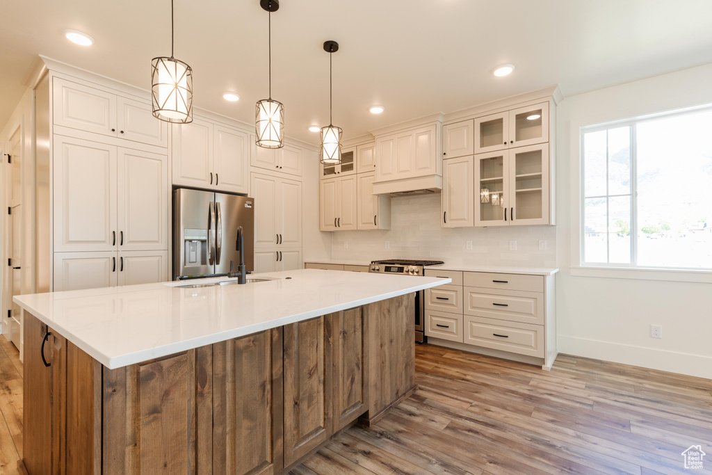Kitchen featuring appliances with stainless steel finishes, baseboards, light wood-style floors, tasteful backsplash, and a center island with sink