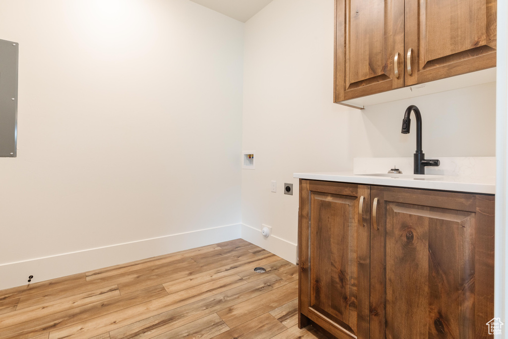 Washroom with electric dryer hookup, cabinet space, light wood-style flooring, baseboards, and hookup for a washing machine
