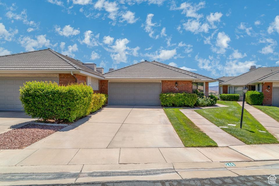 Single story home featuring brick siding, a tiled roof, an attached garage, and concrete driveway