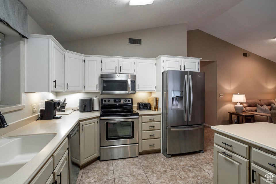 Kitchen with stainless steel appliances, a sink, light countertops, light tile patterned flooring, and white cabinetry