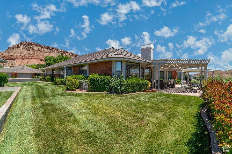 Rear view of house featuring a pergola, a chimney, a lawn, a patio area, and brick siding