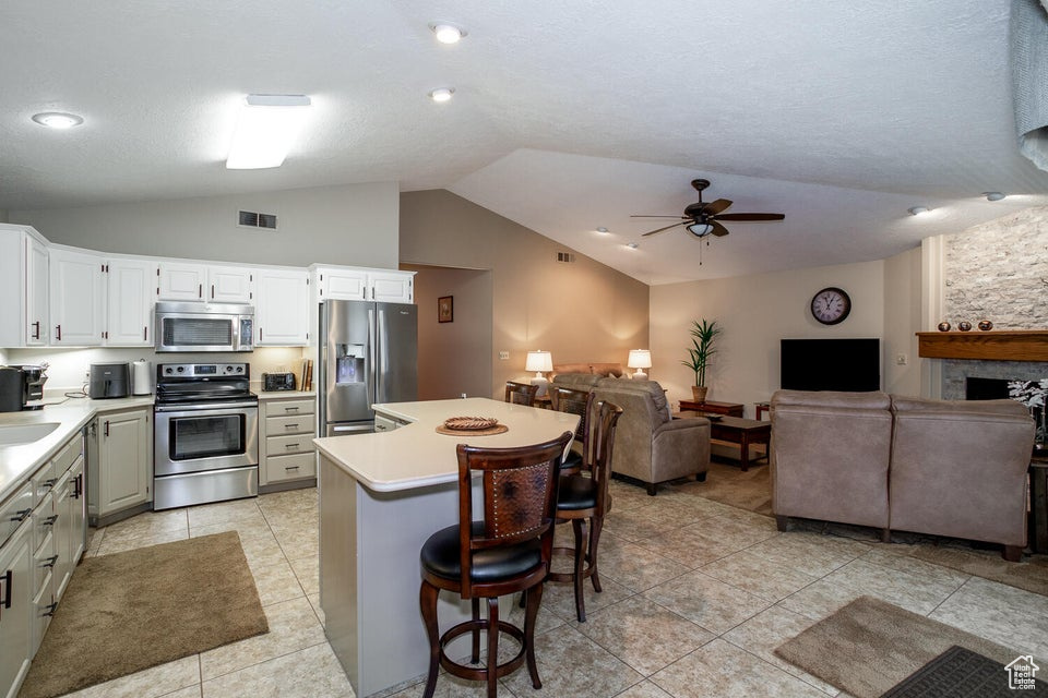 Kitchen featuring appliances with stainless steel finishes, open floor plan, lofted ceiling, a ceiling fan, and a breakfast bar area