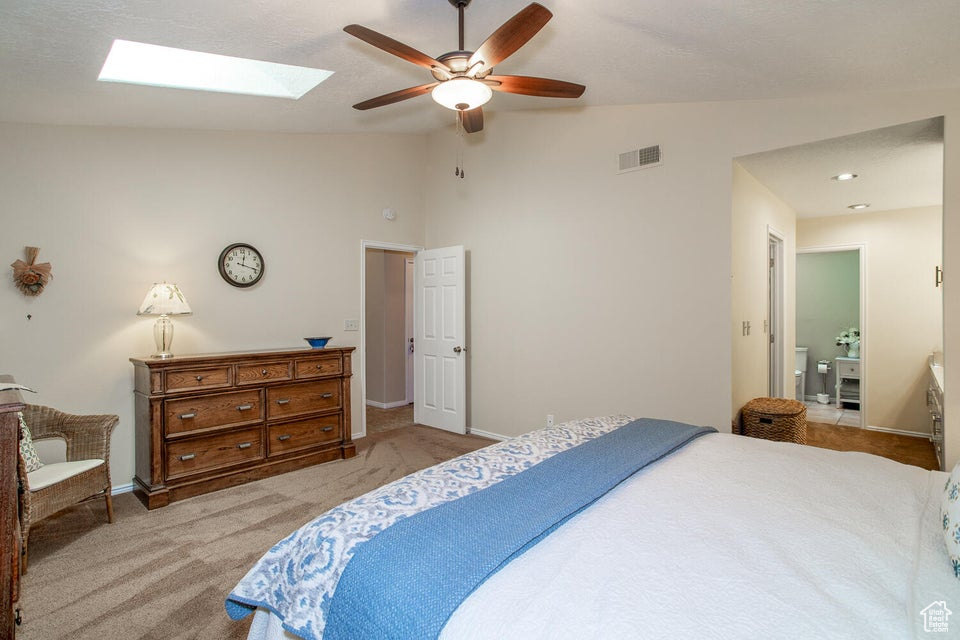 Bedroom featuring vaulted ceiling, light carpet, a skylight, baseboards, and ceiling fan