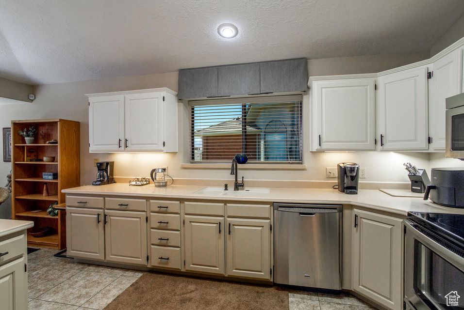 Kitchen featuring appliances with stainless steel finishes, a sink, light countertops, white cabinets, and a textured ceiling