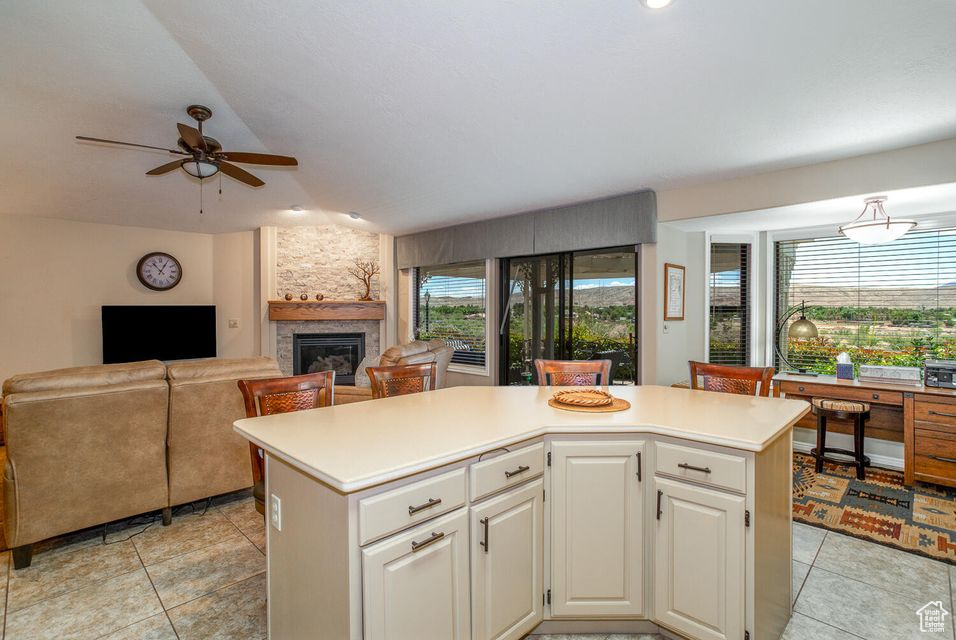 Kitchen featuring ceiling fan, light countertops, a kitchen island, and a stone fireplace