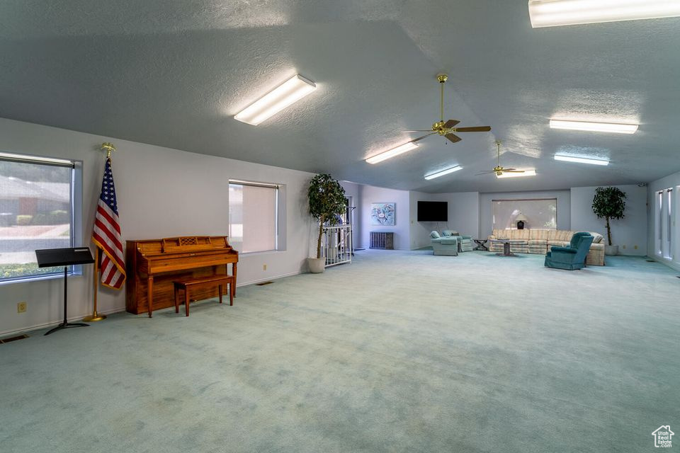 Miscellaneous room featuring ceiling fan, carpet floors, a textured ceiling, vaulted ceiling, and baseboards