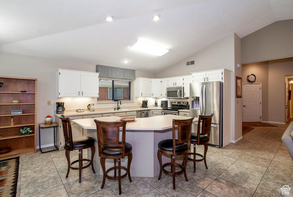 Kitchen featuring stainless steel appliances, lofted ceiling, a sink, light countertops, and a center island