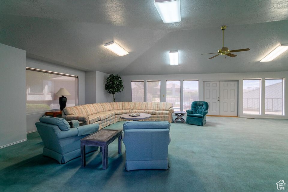 Living room featuring lofted ceiling, carpet, plenty of natural light, a textured ceiling, and a ceiling fan