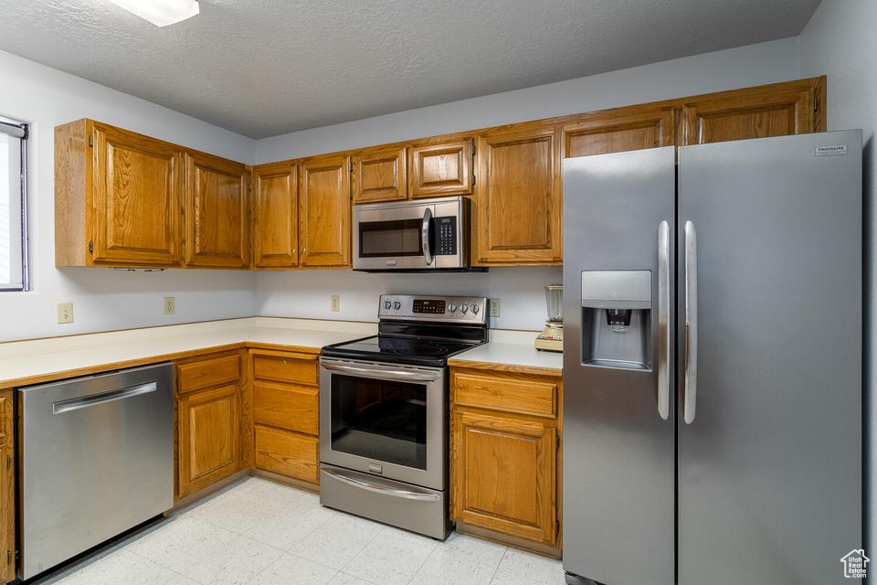 Kitchen with appliances with stainless steel finishes, light countertops, brown cabinetry, and a textured ceiling