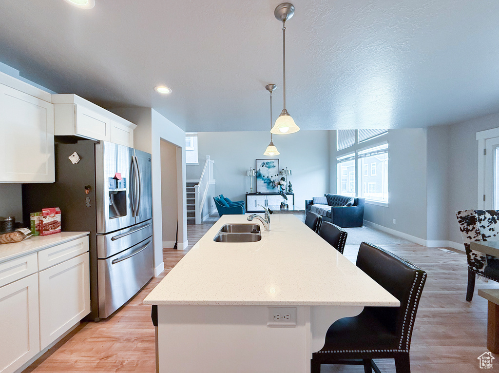 Kitchen with a sink, open floor plan, stainless steel fridge with ice dispenser, a kitchen bar, and baseboards