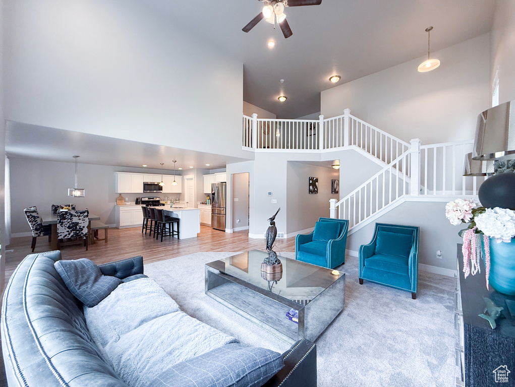Living area with a ceiling fan, stairway, high vaulted ceiling, and baseboards